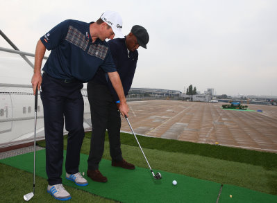 Justin Rose coaches Ian Wright to play a shot from the wing of a British Airways Boeing 747